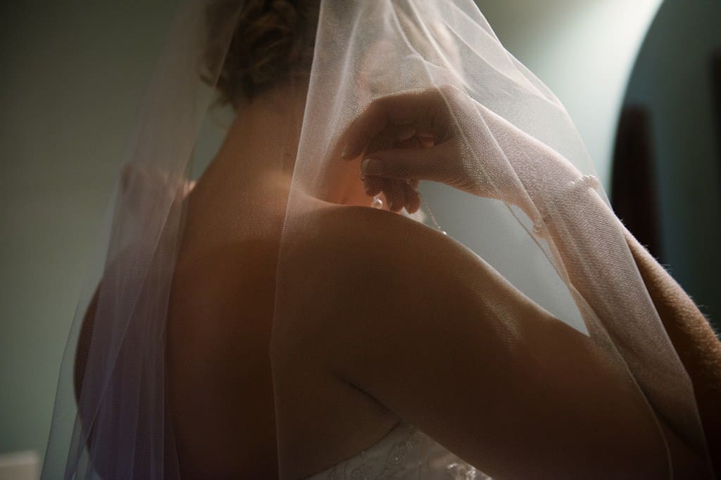 bride putting on necklace beneath veil