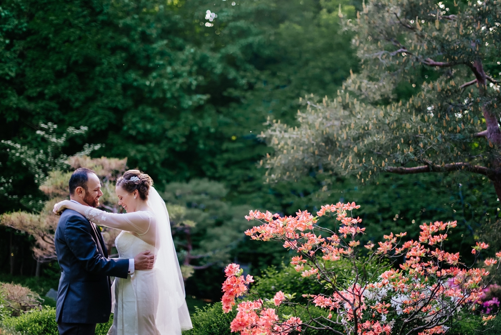 bride and groom embrace in arboretum in front of pink flowers