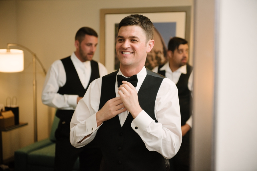 Groom arranging his bowtie in front of a mirror