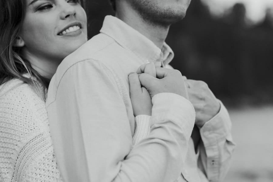 newly engaged couple embraces beside lake superior