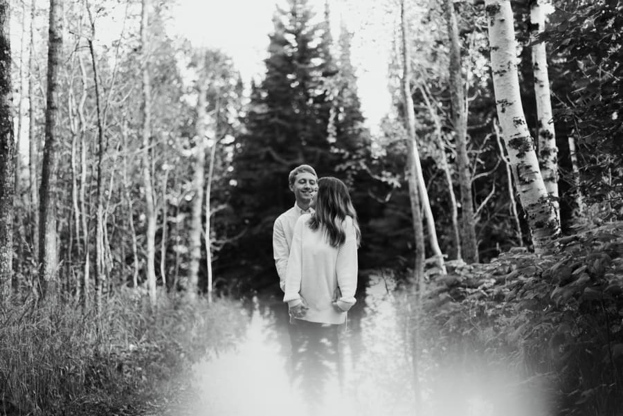 couple embraces in woods with bright reflection at bottom