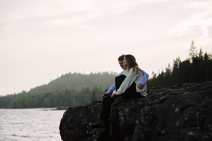 couple sits lakeside during sunset engagement session