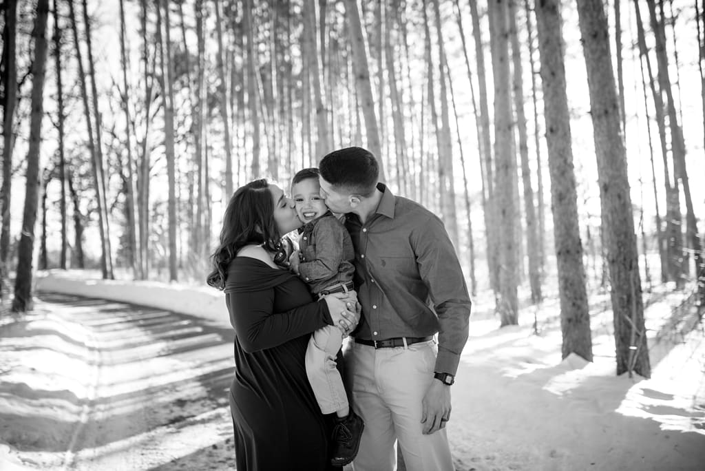 expecting couple kisses older child in snow