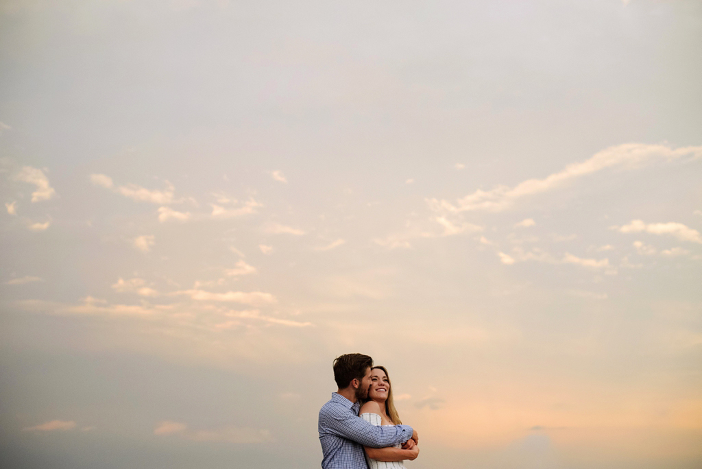 couple embracing in front of sunset sky with clouds