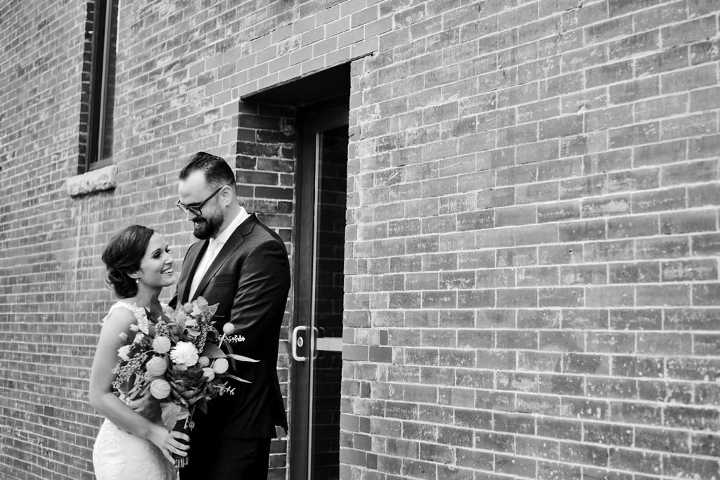 bride and groom with bouquet outside brick building