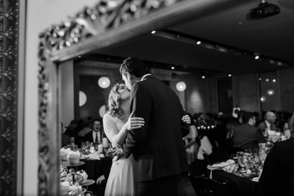 reflection in mirror of bride and groom kissing at wedding reception