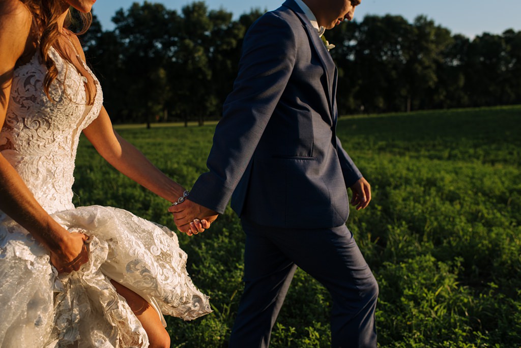 newlyweds walk hand in hand through field