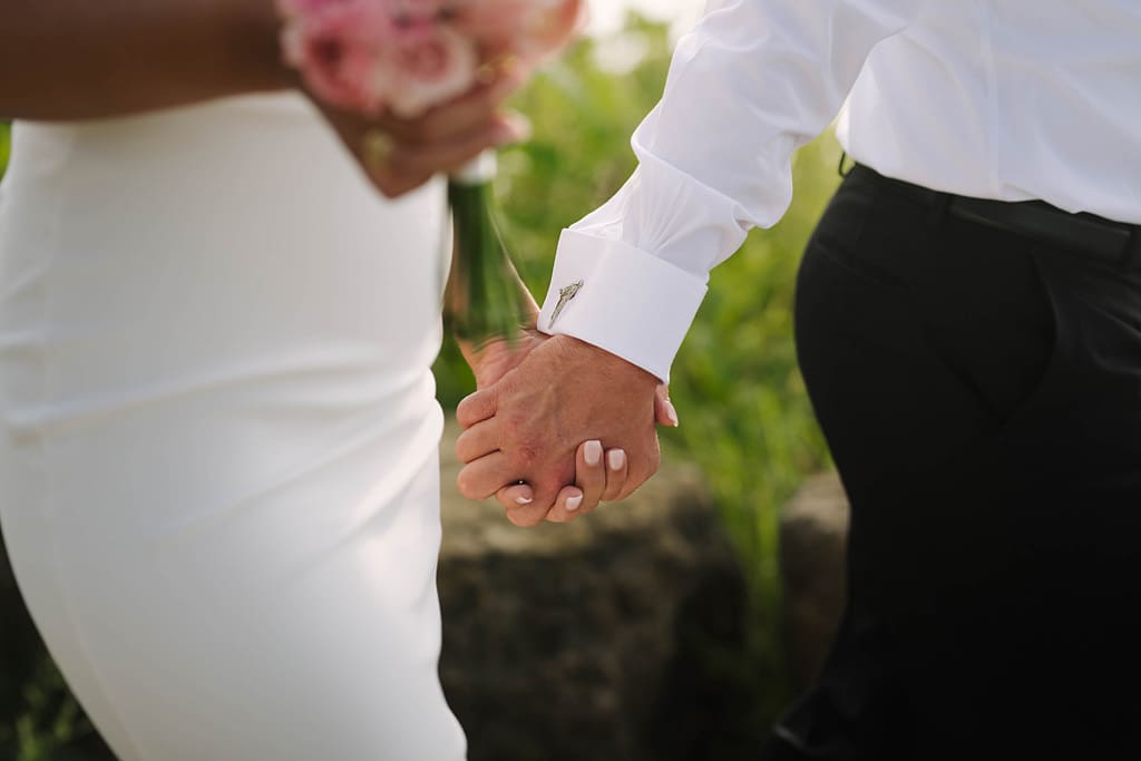 detail of bride and groom holding hands with pistol cufflinks