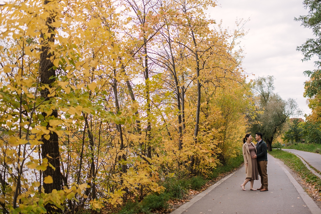 expecting parents on a park path in front of yellow fall trees