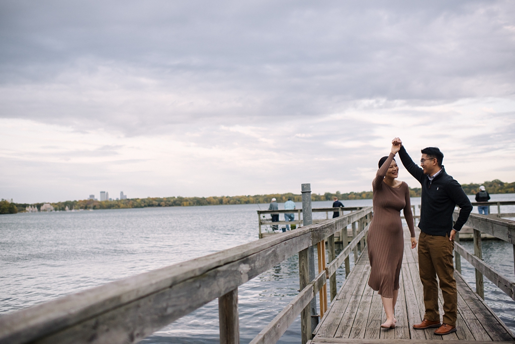 pregnant couple dancing on lakeside pier with minneapolis skyline