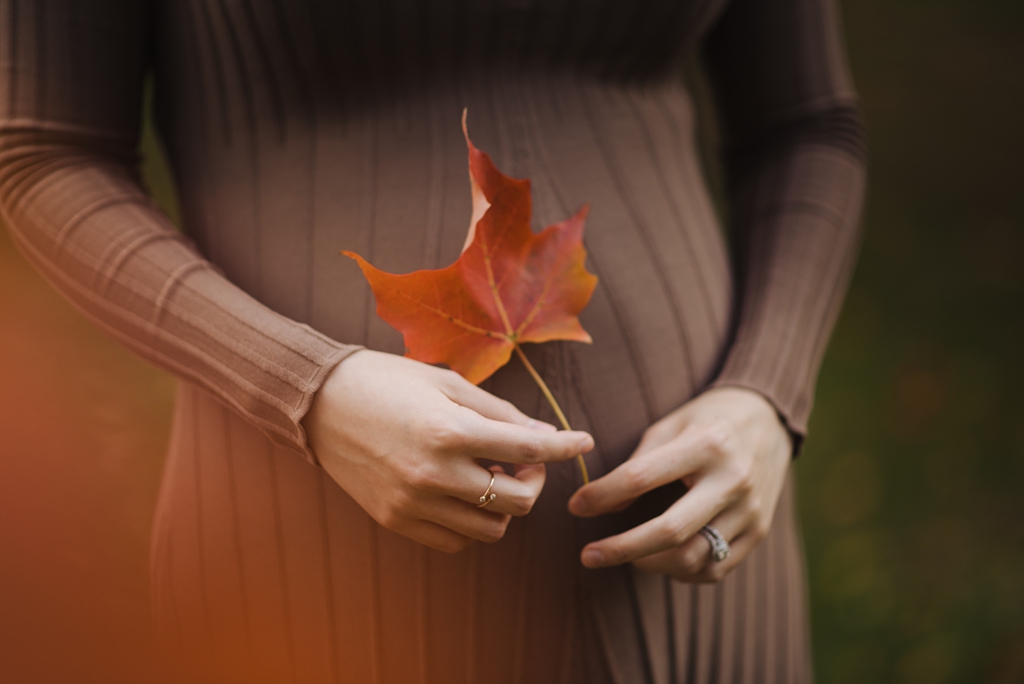 expectant mother holding orange fall leaf over belly