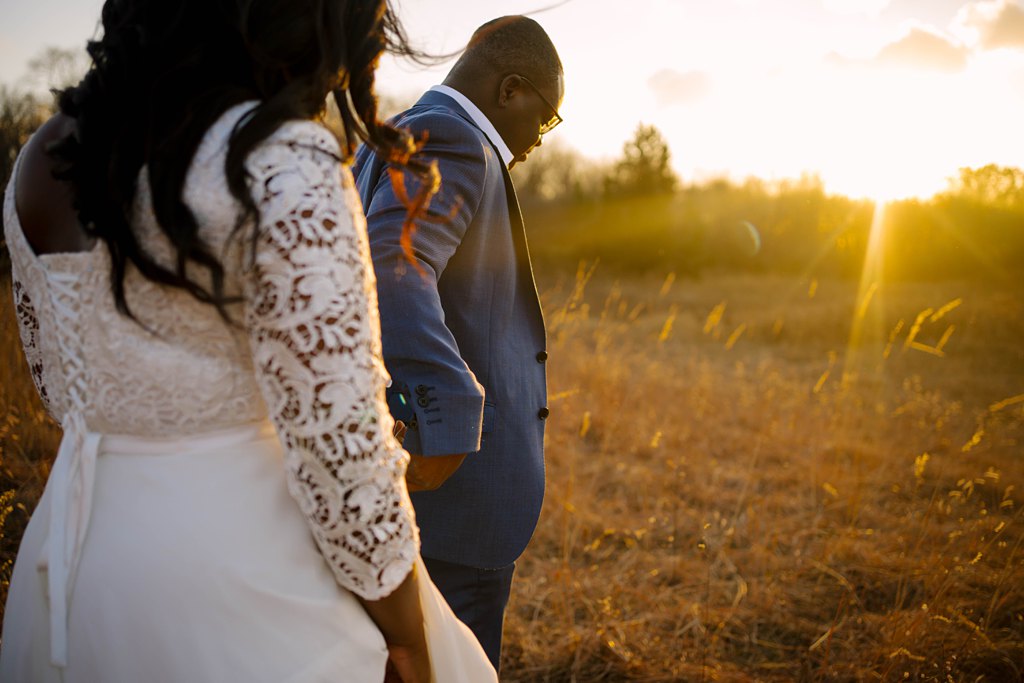 newlywed couple walking through field toward setting sun