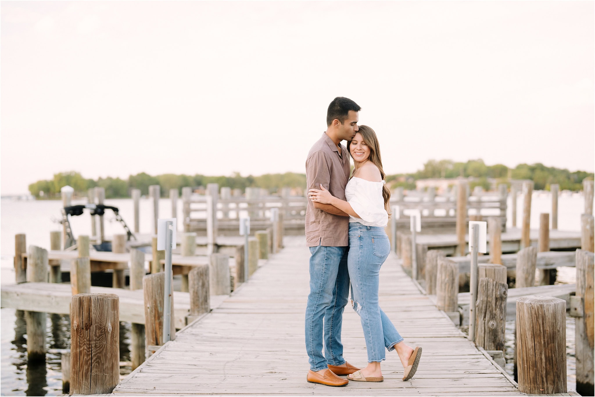 A man kissing his fiancé on the forehead while embracing on the pier at Port Excelsior.