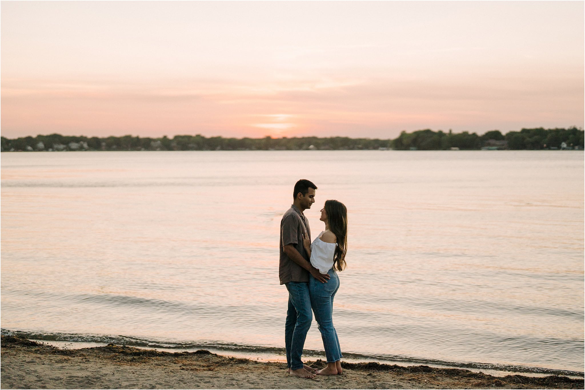 A serene view of the lake at Port Excelsior with an engaged couple in the center shot, smiling at each other, their bodies in a close embrace.