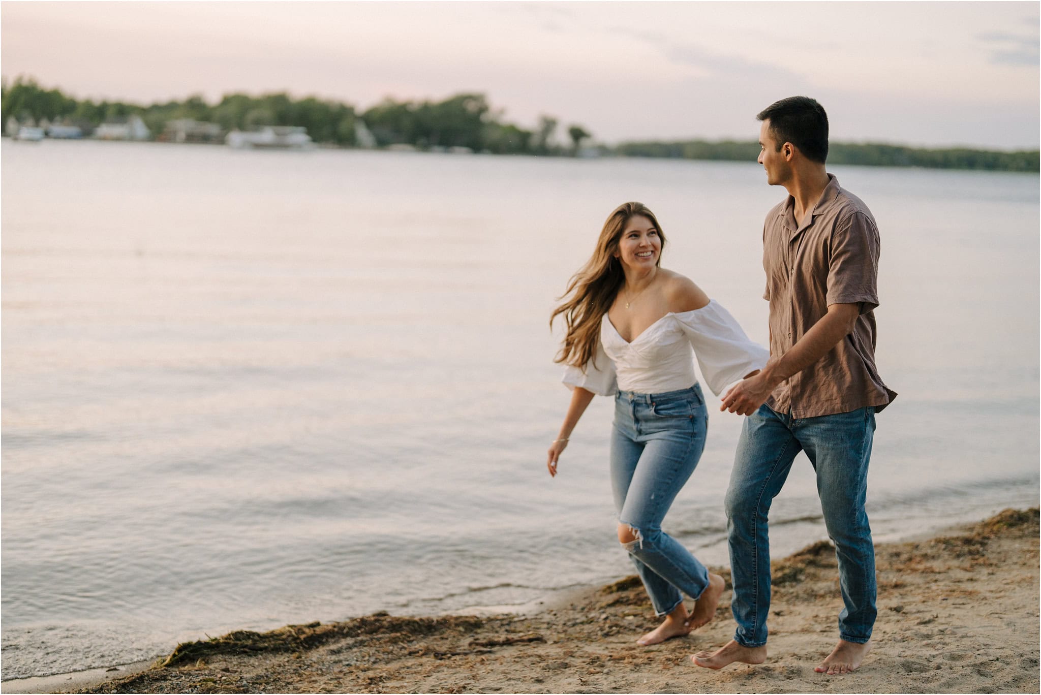 An engaged couple walking hand in hand down the shore at Port Excelsior while the gold hour light illuminates them.