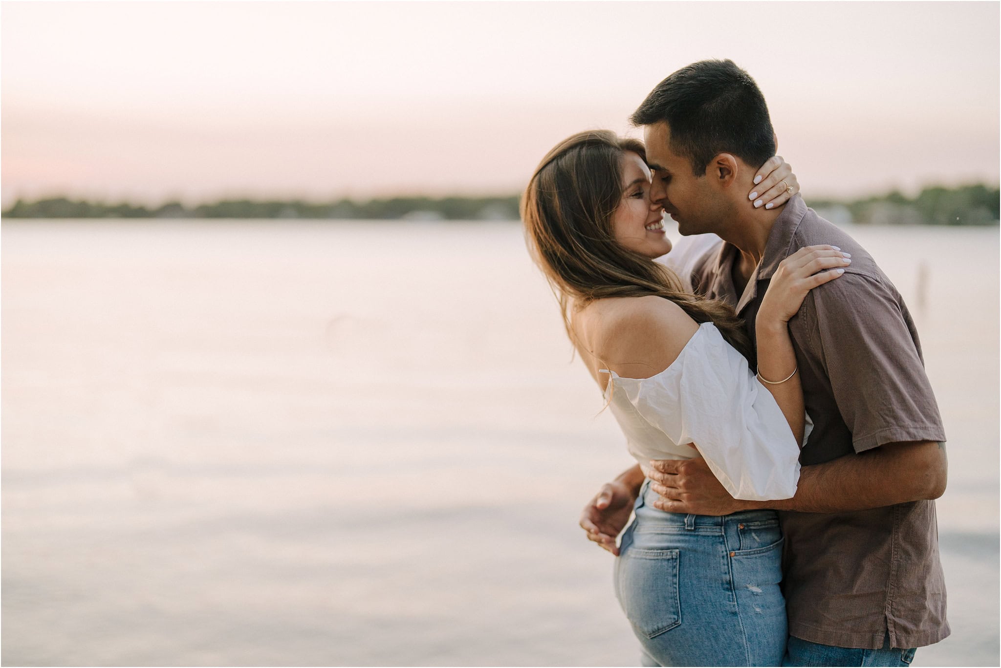 A close-up of an engaged couple embracing after a passionate kiss, the lake at Port Excelsior behind them.